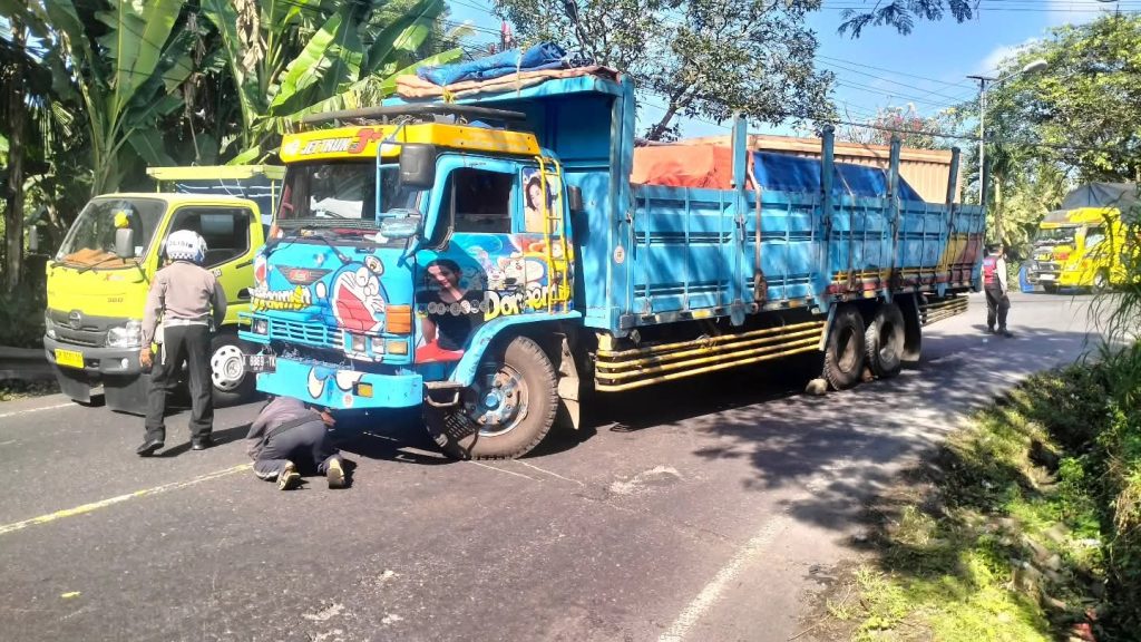 Petugas Polsek Selemadeg bersama teknisi melakukan penanganan truk tronton bermuatan keramik yang mengalami kerusakan per stir di jalur utama Denpasar-Gilimanuk, simpang Banjar Sukawati, Kecamatan Selemadeg, Tabanan, Selasa (5/8/2025). Insiden ini sempat menyebabkan kemacetan panjang sebelum akhirnya arus lalu lintas kembali normal. (Foto: Istimewa)