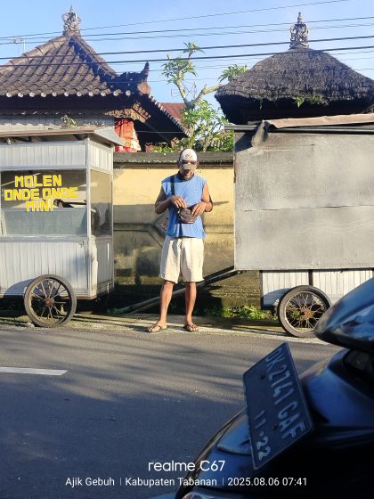 Seorang pedagang kaki lima sedang bersiap membuka lapak jajanan tradisional molen onde-onde mini di pinggir jalan kawasan Kabupaten Tabanan, Bali, saat pagi hari. Fenomena pedagang keliling seperti ini masih menjadi pemandangan khas di banyak daerah Bali. (Foto: Istimewa)